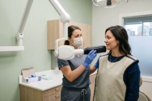 Patient reclined in a dental chair while a hygienist performs a routine teeth cleaning.